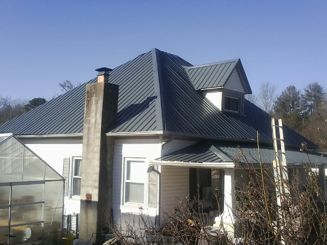 Dark blue standing seam metal roof on a white farmhouse with dormer — Slate & Tile Roof Repair by Roofing Brothers in Lanexa