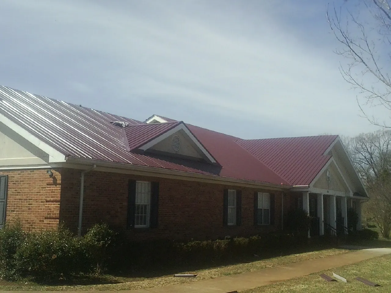 Red metal roof with gabled entries on a long brick building, from a Hail Damage Roof Repair job in Lanexa