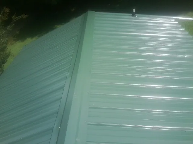 New green metal panels meeting at the ridge of a roof — Flat Roof Repair work by our crew in Lanexa