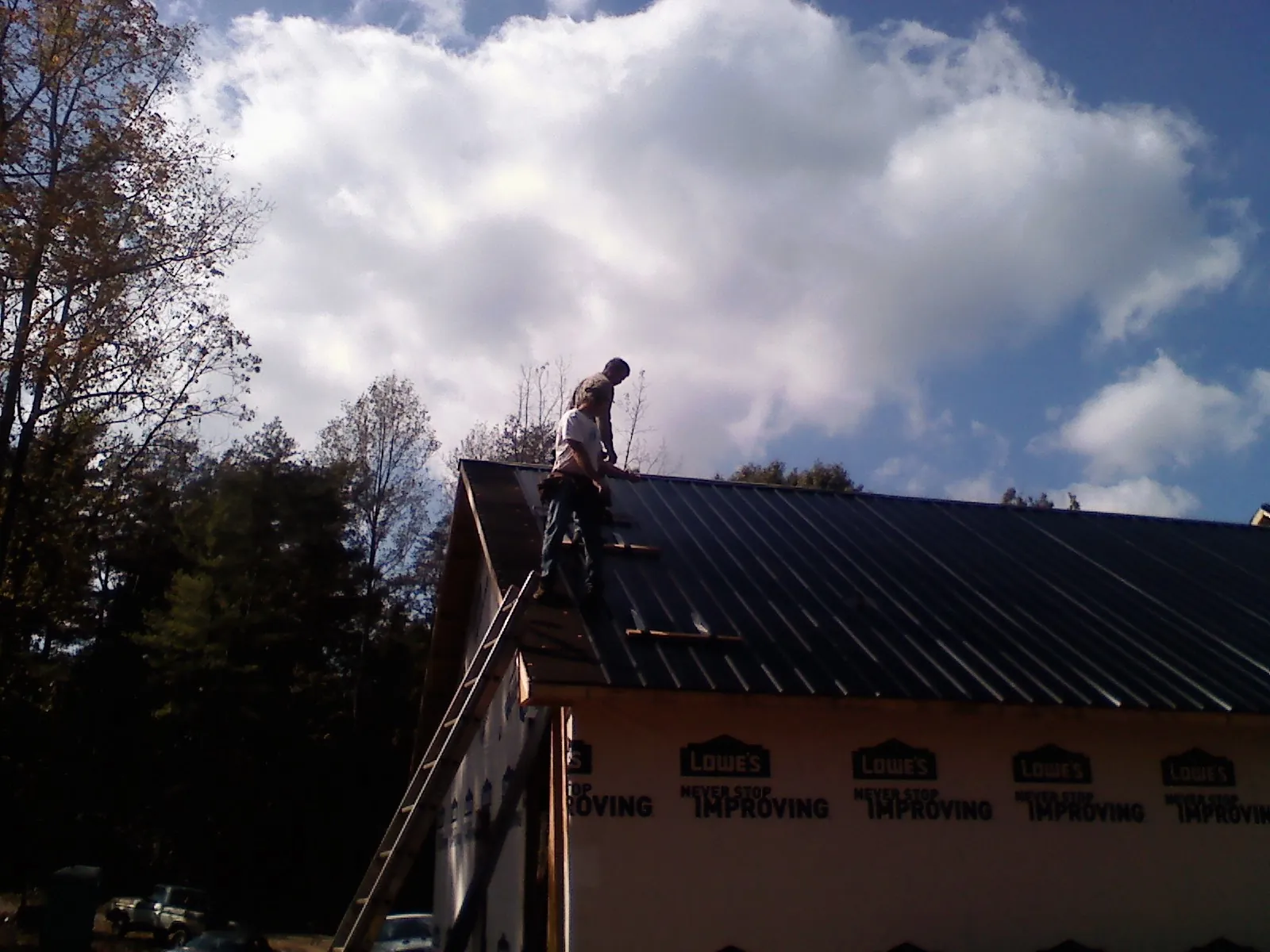 Roofer fastening dark metal panels high against a cloudy sky, from a Roof Inspection job in Lanexa